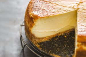Baked cheesecake with a golden top and thick creamy interior, shown with one large slice removed to reveal its smooth texture and graham cracker crust.