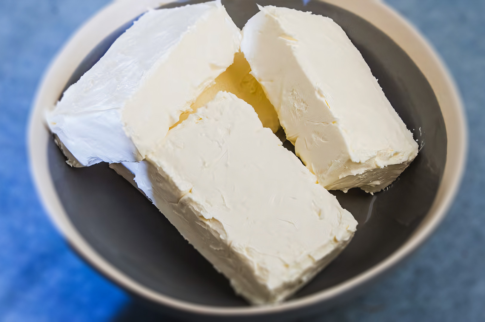 Four blocks of cream cheese placed in a ceramic bowl, showing their smooth, dense texture before mixing.