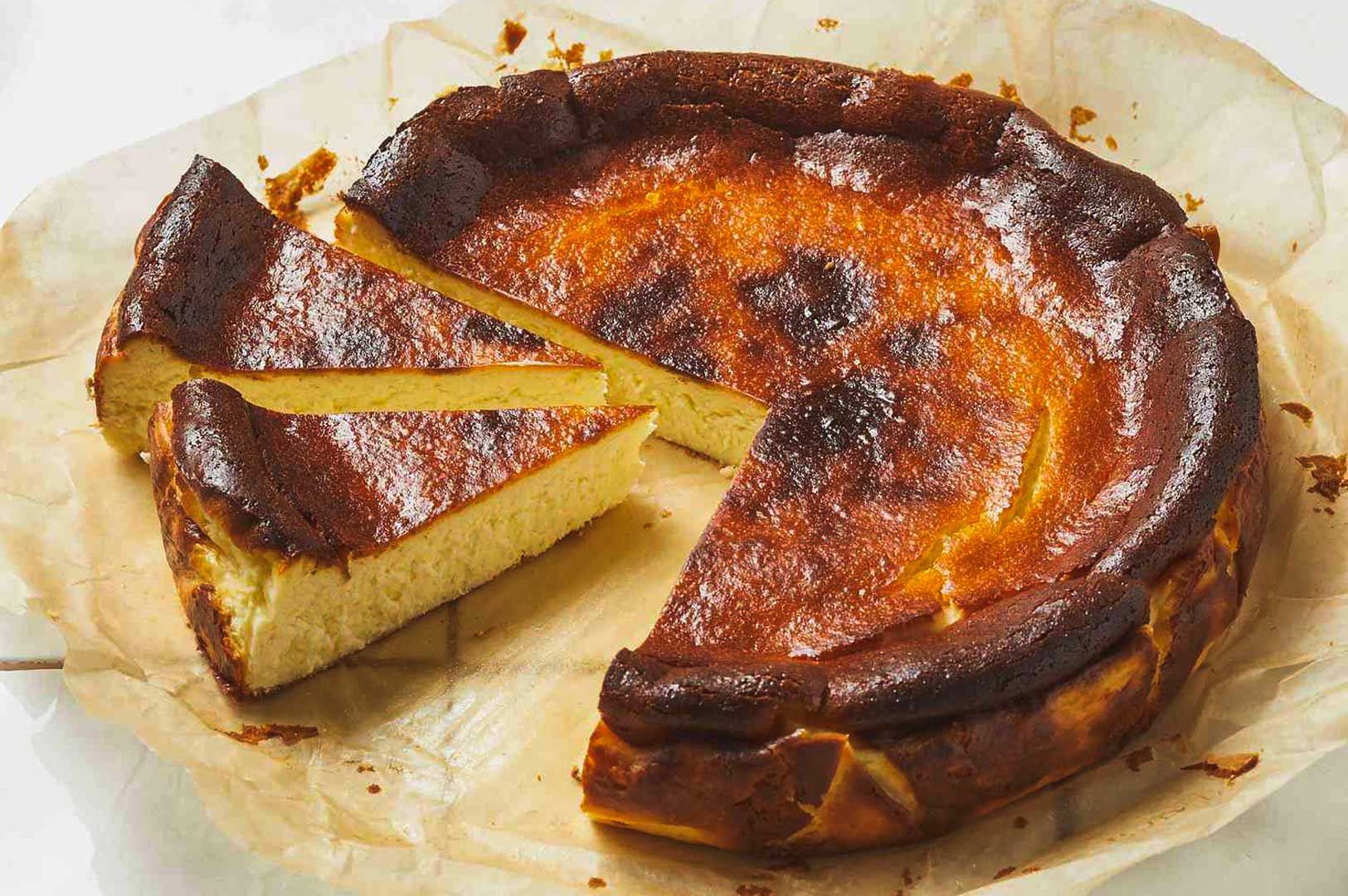 Burnt Basque cheesecake on parchment paper with two slices cut out, showing the creamy interior and caramelized top.