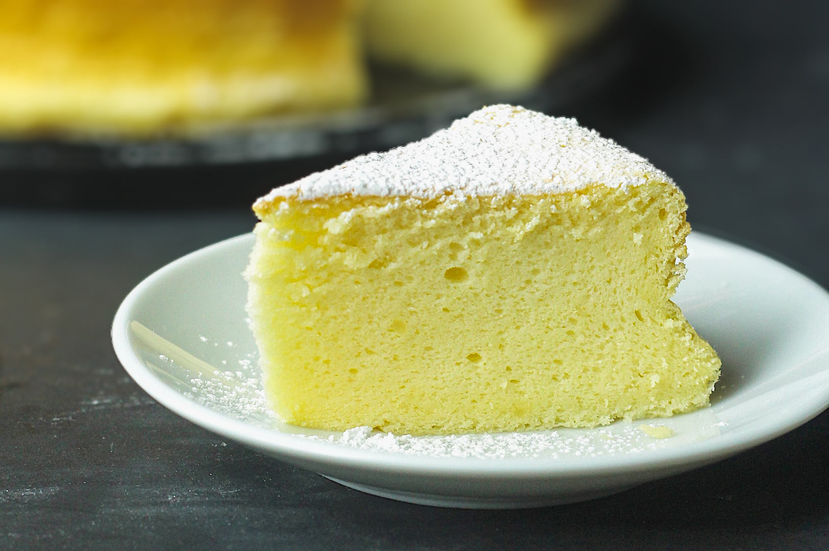 Slice of Japanese cotton cheesecake on a white plate, showing its light and airy texture with a dusting of powdered sugar.