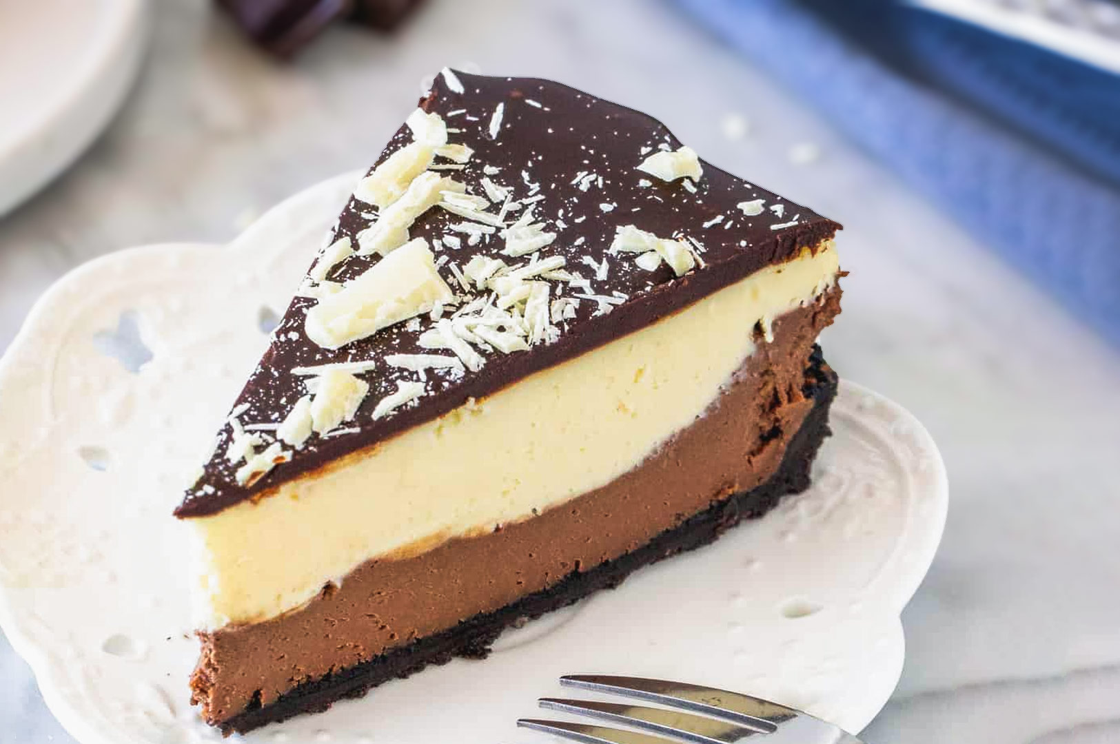 Three-layer chocolate cheesecake slice with dark chocolate ganache and white chocolate shavings on top.