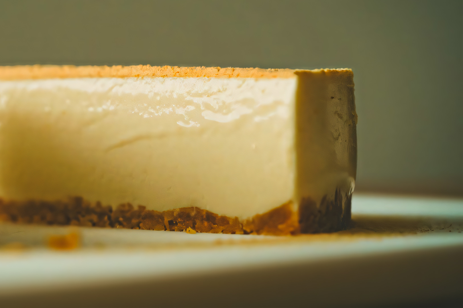 Close-up of a smooth no-bake cheesecake slice with a golden graham cracker crust on a white plate, highlighting its creamy texture.