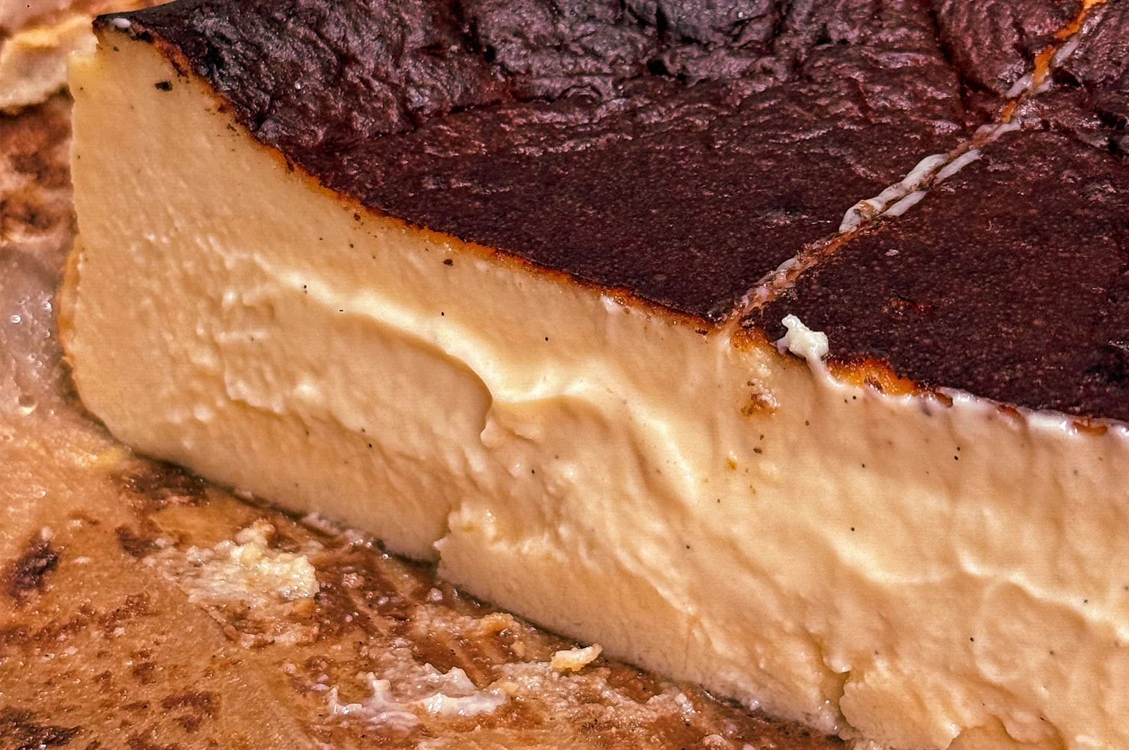 Close‑up of a sliced Basque cheesecake showing creamy interior and signature dark burnt top.