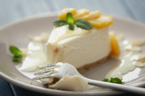 A slice of lemon cheesecake topped with lemon slices and fresh mint, served with a fork on a white plate