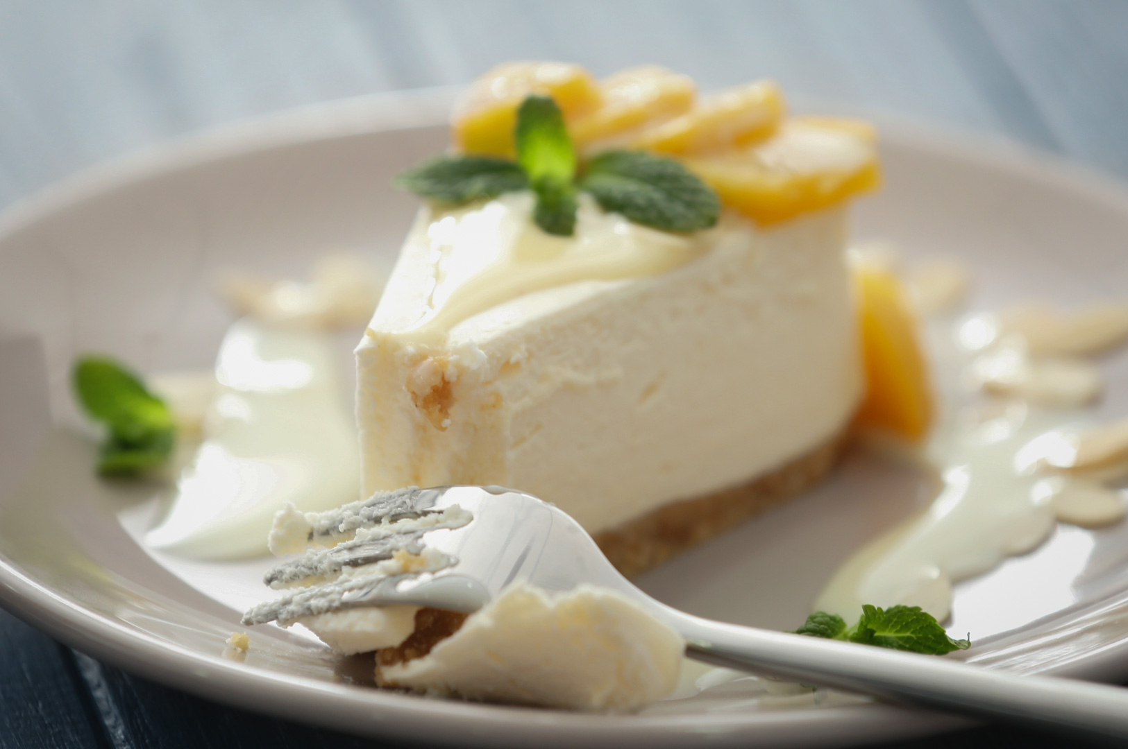 A slice of lemon cheesecake topped with lemon slices and fresh mint, served with a fork on a white plate