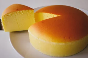 Side-angle shot of a fluffy Japanese soufflé cheesecake on a white plate, with one slice removed to reveal a soft, airy interior and evenly baked golden top.