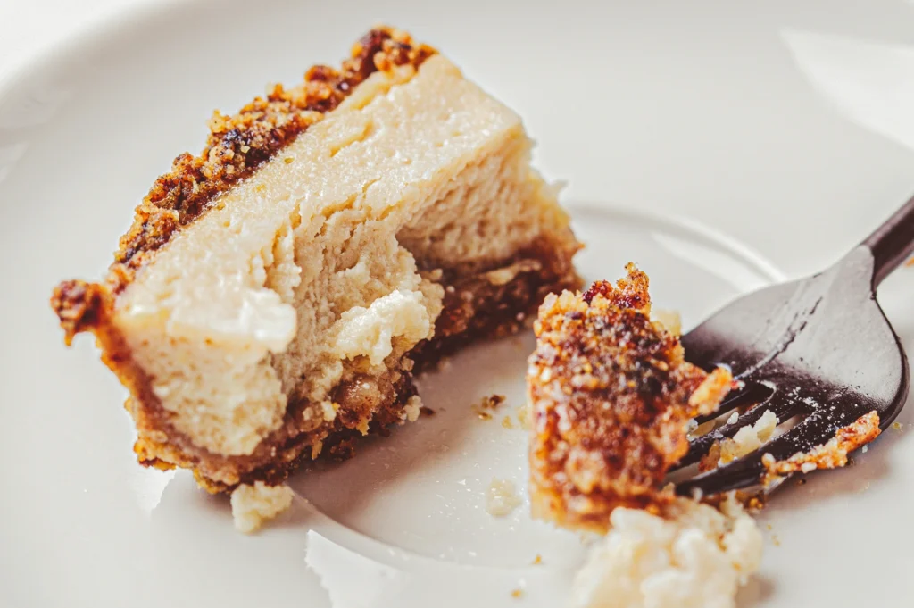 Partially eaten cheesecake with a crumbly biscuit base and creamy interior, served on a white plate to showcase the dessert’s texture and layers