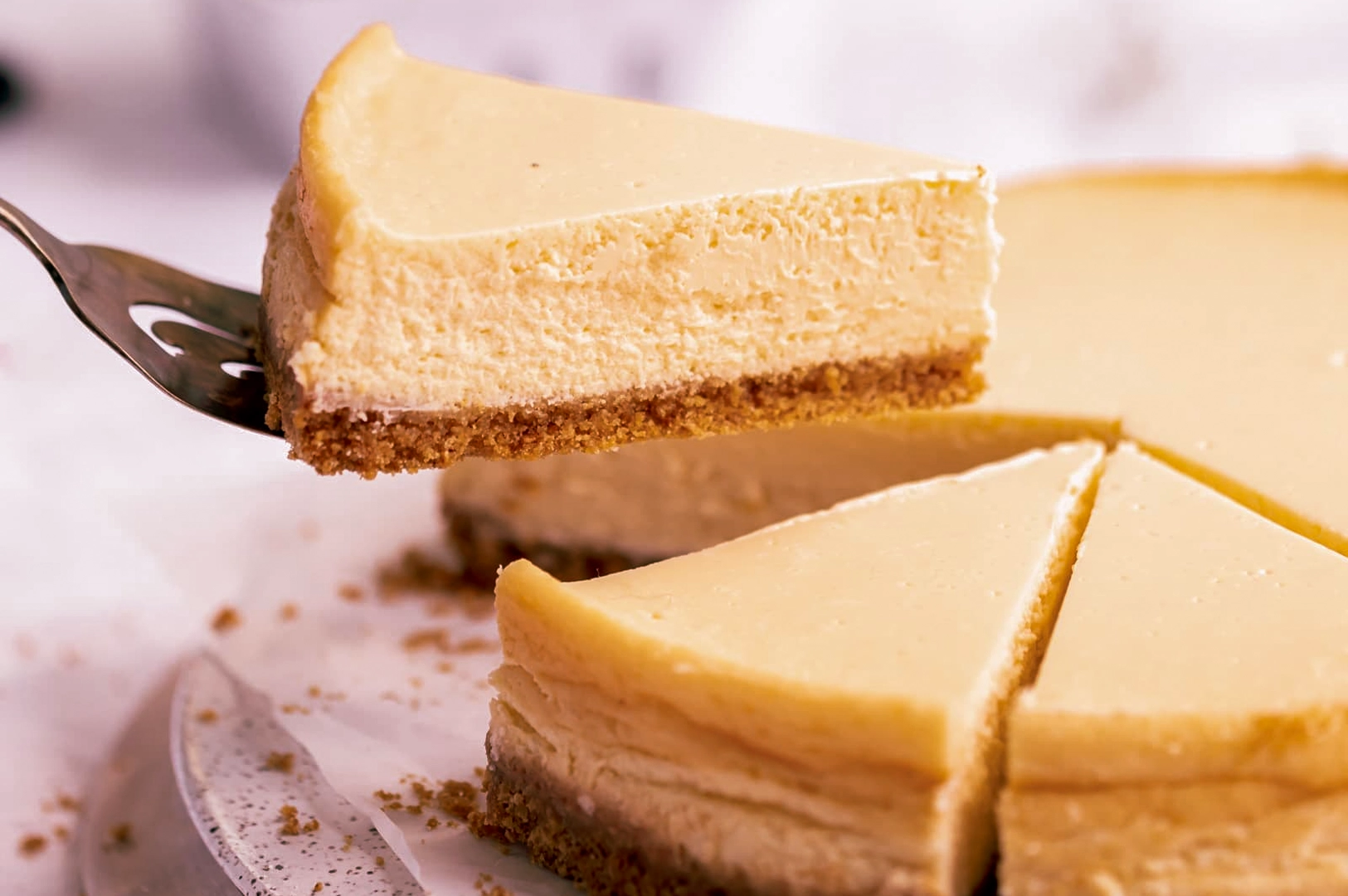 Creamy New York–style cheesecake slice lifted with a spatula, showing smooth filling and crumb crust
