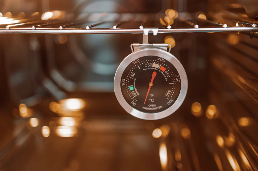 Oven thermometer hanging inside an oven, showing temperature readings used for baking Basque burnt cheesecake accurately