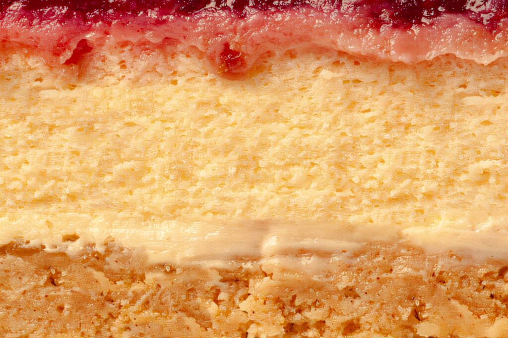 Extreme close‑up of cheesecake layers showing graham crust, creamy filling, and a strawberry topping