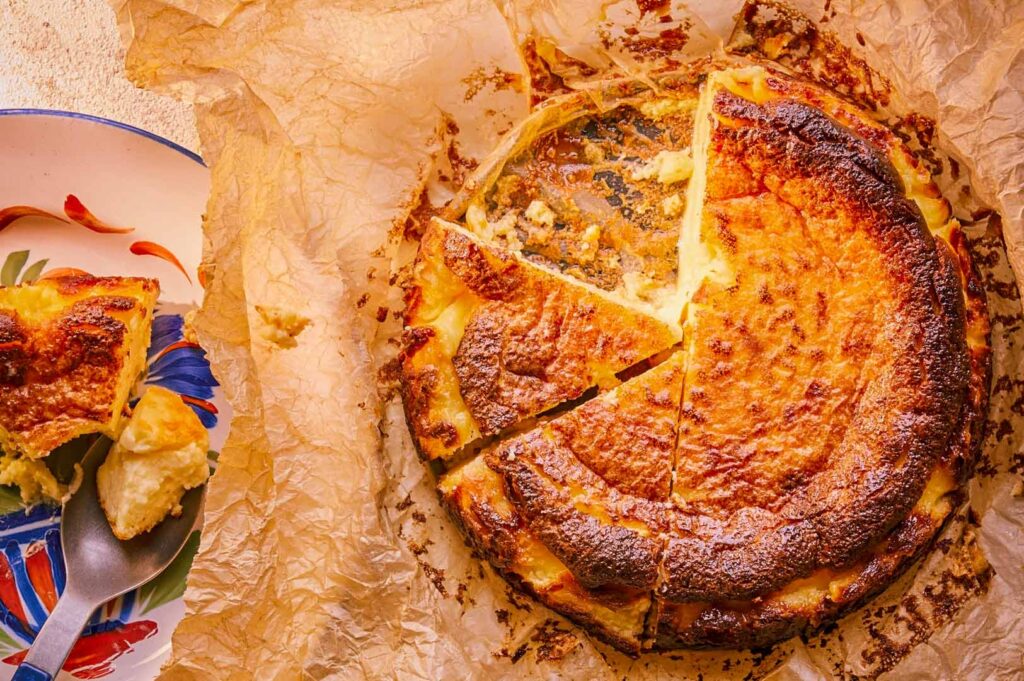 Whole Basque burnt cheesecake with a caramelized top sliced open on parchment paper.