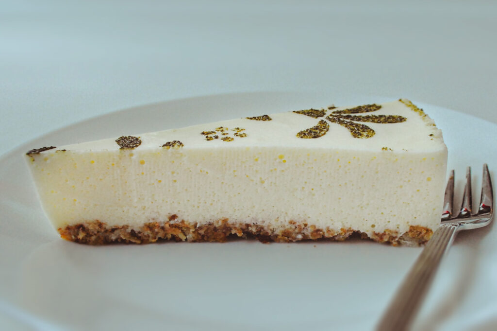 A slice of light, smooth cheesecake with a biscuit crust and decorative powdered topping on a white plate