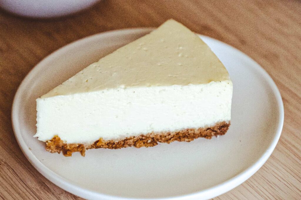 A slice of classic cheesecake with a golden-brown crust served on a simple white plate