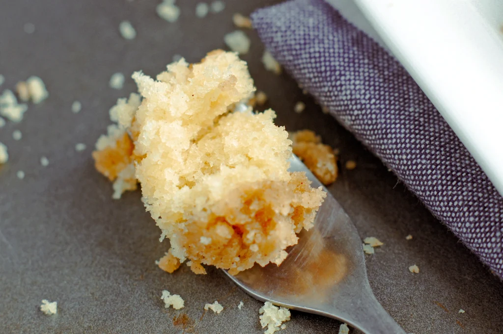 Macro close‑up shot of a spoon holding soft cake crumbs with golden crust texture on a dark surface, highlighting dessert details and crumb structure.