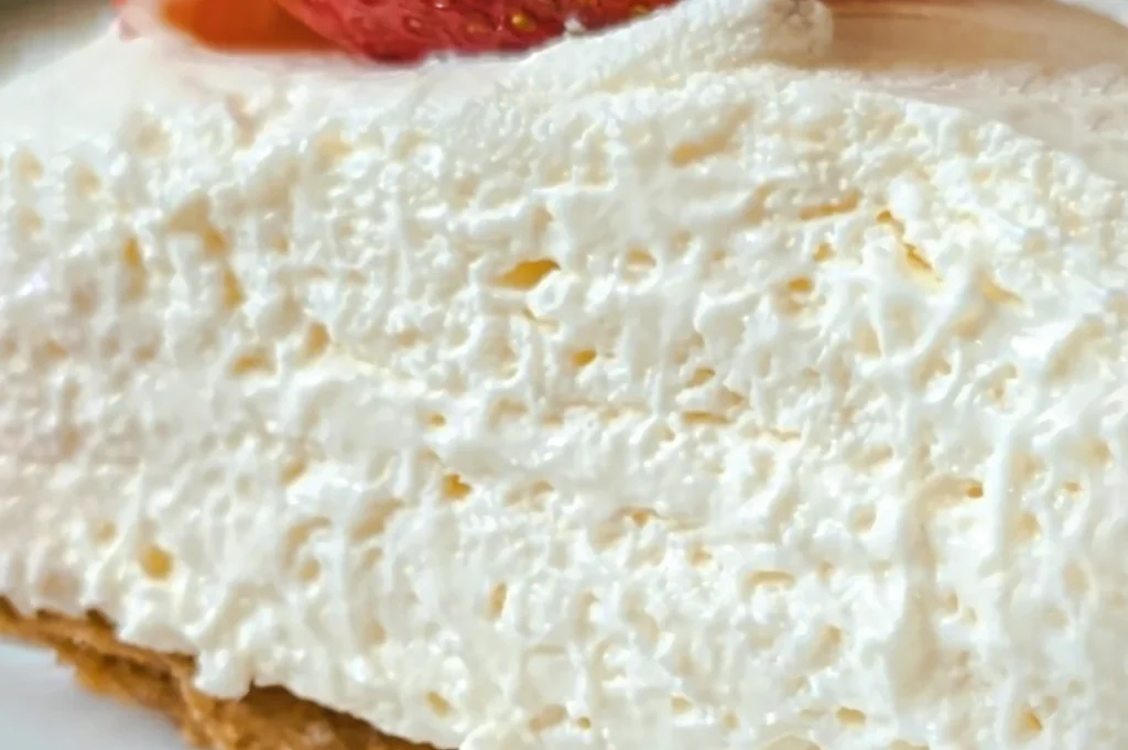 Close‑up of a creamy, fluffy non-baked cheesecake slice with a smooth whipped texture and a strawberry garnish on top