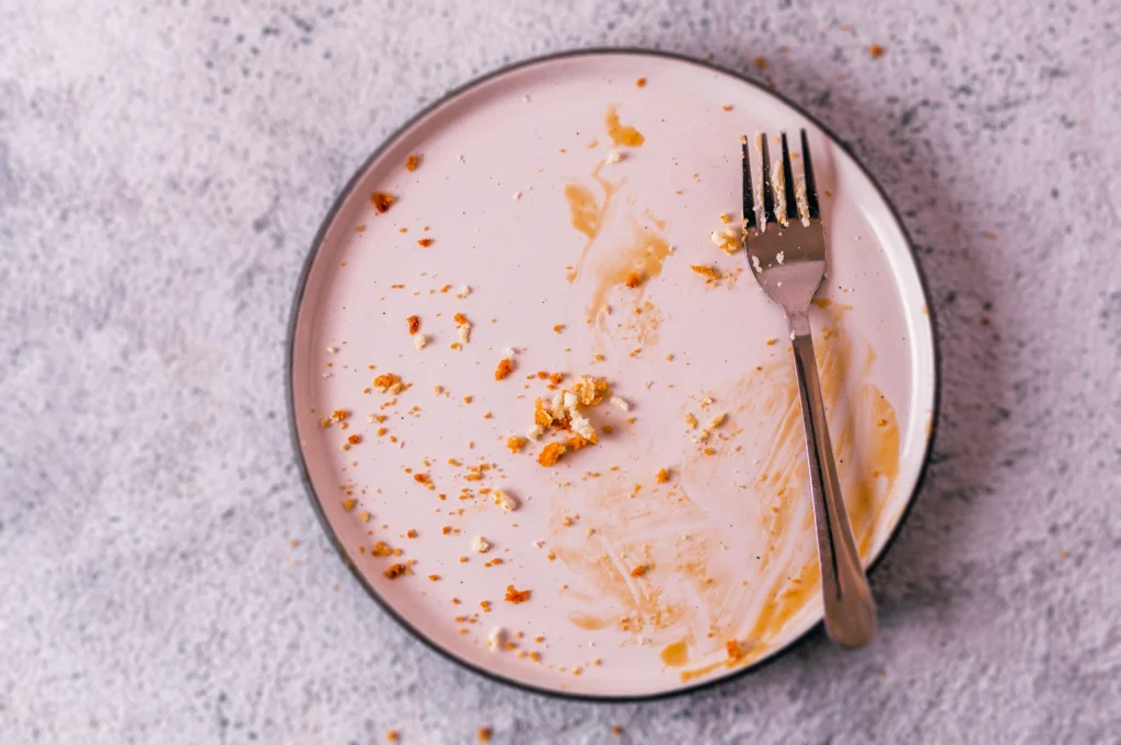 Empty dessert plate with cheesecake crumbs and a fork, showing the final moments after finishing a cheesecake slice.