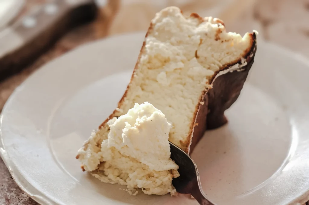 Slice of Basque burnt cheesecake on a white plate with a spoonful taken out, showing its soft, creamy filling and dark caramelized crust
