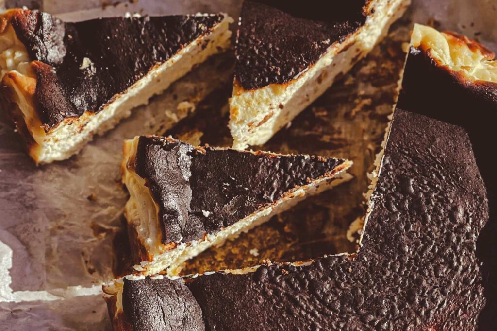 Slices of burnt Basque cheesecake with a dark caramelized top and creamy interior arranged on parchment paper