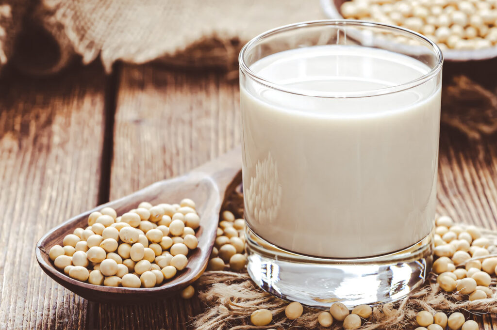 A glass of fresh soy milk surrounded by raw soybeans on a rustic wooden table.