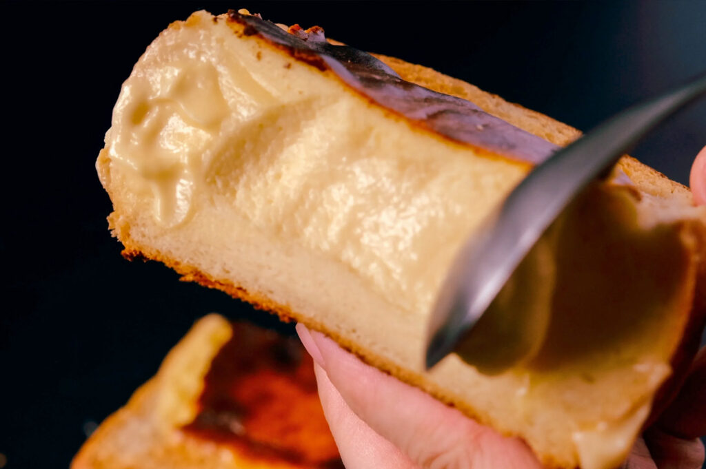 Close-up of a creamy molten cheesecake slice with a caramelized top being scooped with a spoon.
