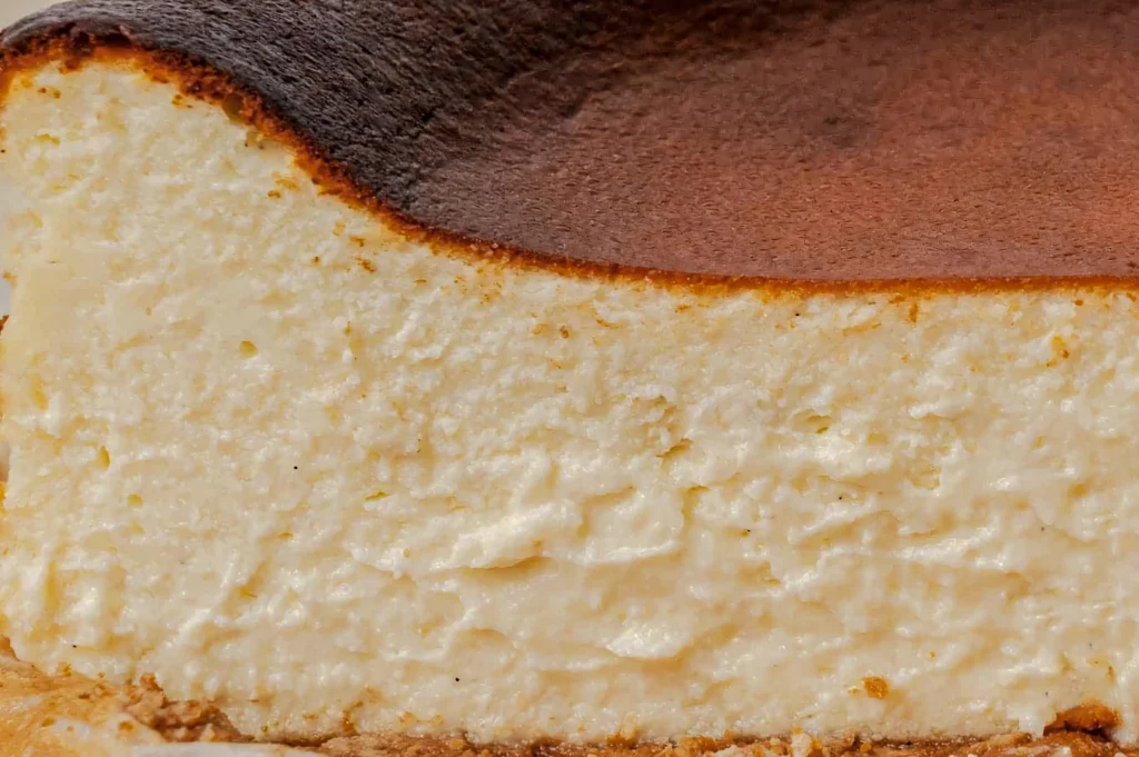 Creamy interior cross‑section of a Basque burnt cheesecake with a golden, deeply browned top and smooth custard-like texture