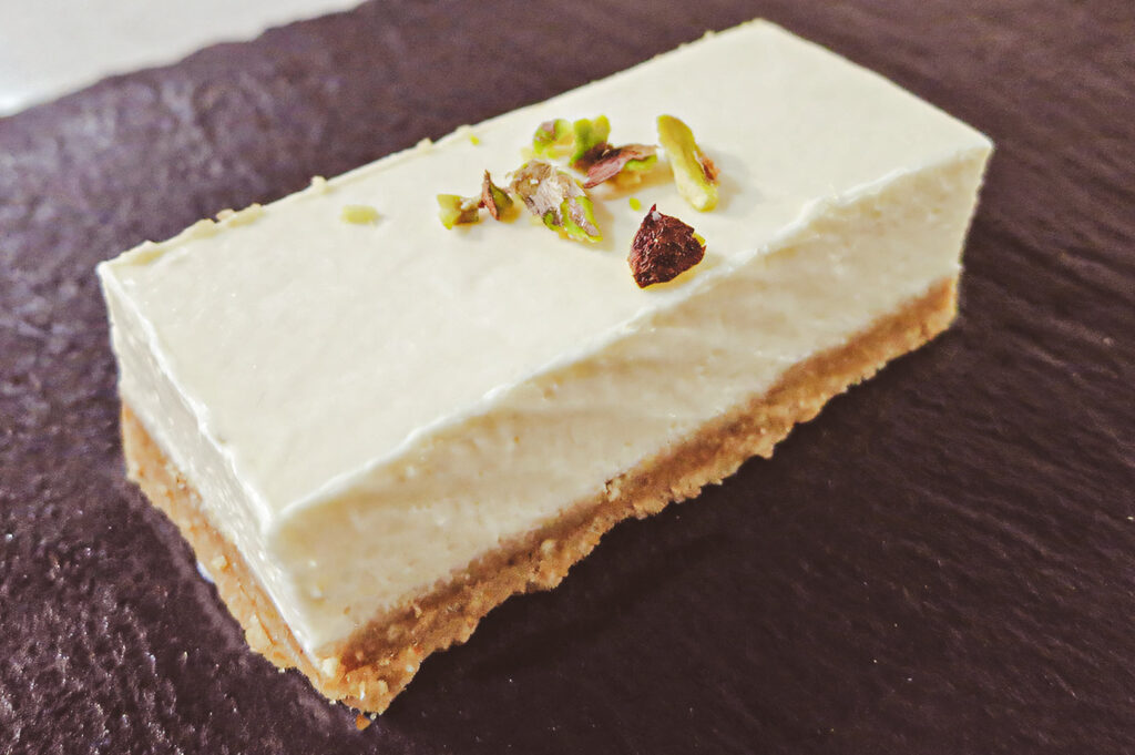 A rectangular tofu cheesecake bar with a crumb crust, topped with chopped nuts for garnish.