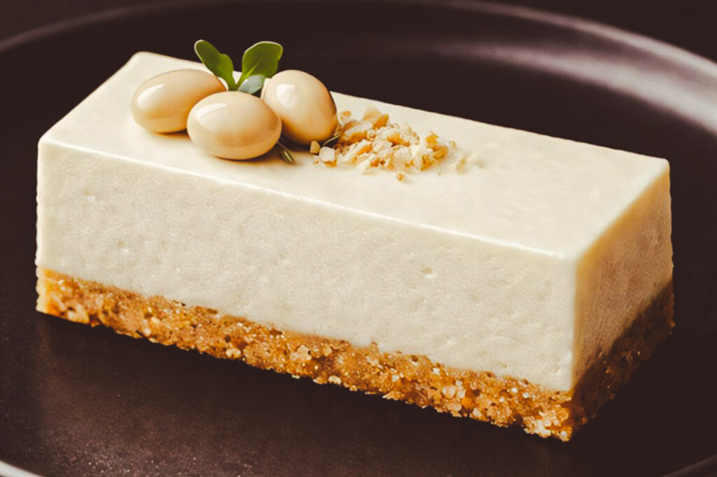 A rectangular soy cheesecake bar with a crunchy crust, garnished with whole soybeans and crushed nuts