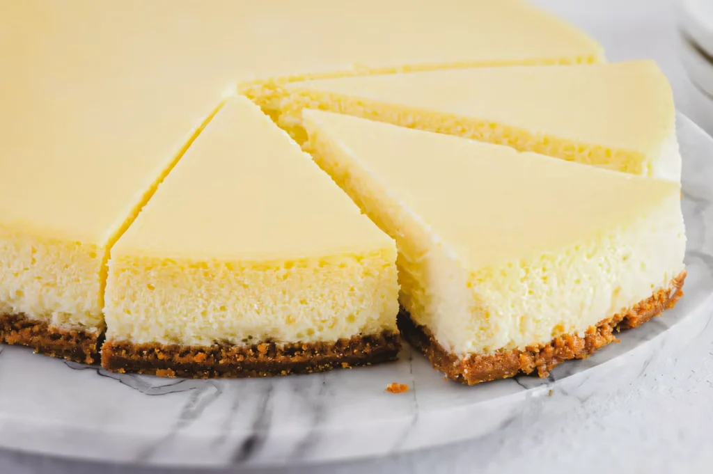 Eye-level close-up of sliced baked cheesecake on a plate, showing a smooth, creamy interior achieved using the water bath baking method.
