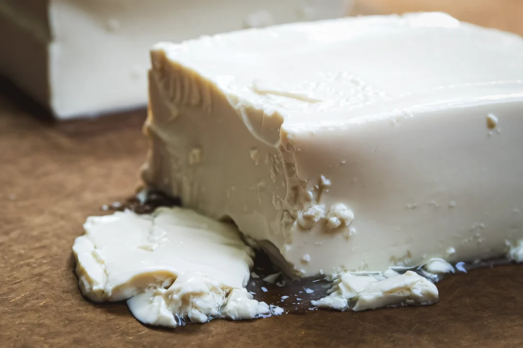 Macro close-up side-angle shot of silken tofu showing a smooth, custard-like soy texture with soft edges and natural moisture pooling on a brown surface.