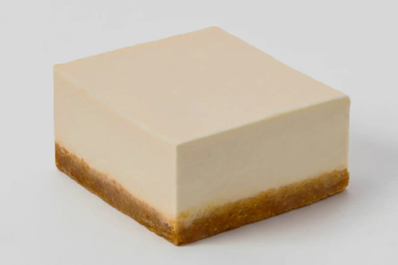 A square slice of creamy cheesecake with a smooth, pale top layer and a dense, brown graham cracker crust at the bottom. The background is pure white.