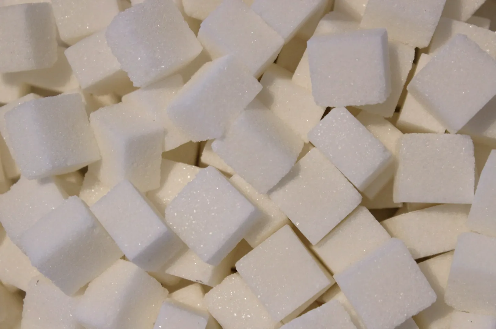 A close-up image of numerous white sugar cubes piled together, creating a textured surface. The cubes vary slightly in angle, enhancing depth.