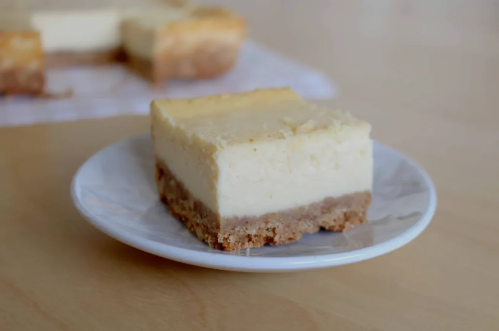 A slice of creamy cheesecake with a golden-brown crust sits on a white plate. The focus is on its smooth texture, evoking a sense of indulgence.