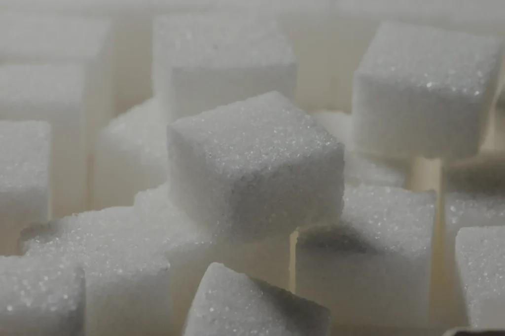 Close-up image of white sugar cubes stacked randomly, showing their rough, granular texture. The tone is neutral and straightforward.