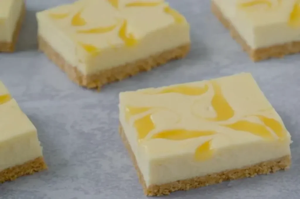 Close-up of lemon swirl cheesecake bars on parchment paper. Each square features a creamy lemon layer with swirls atop a crumbly crust.