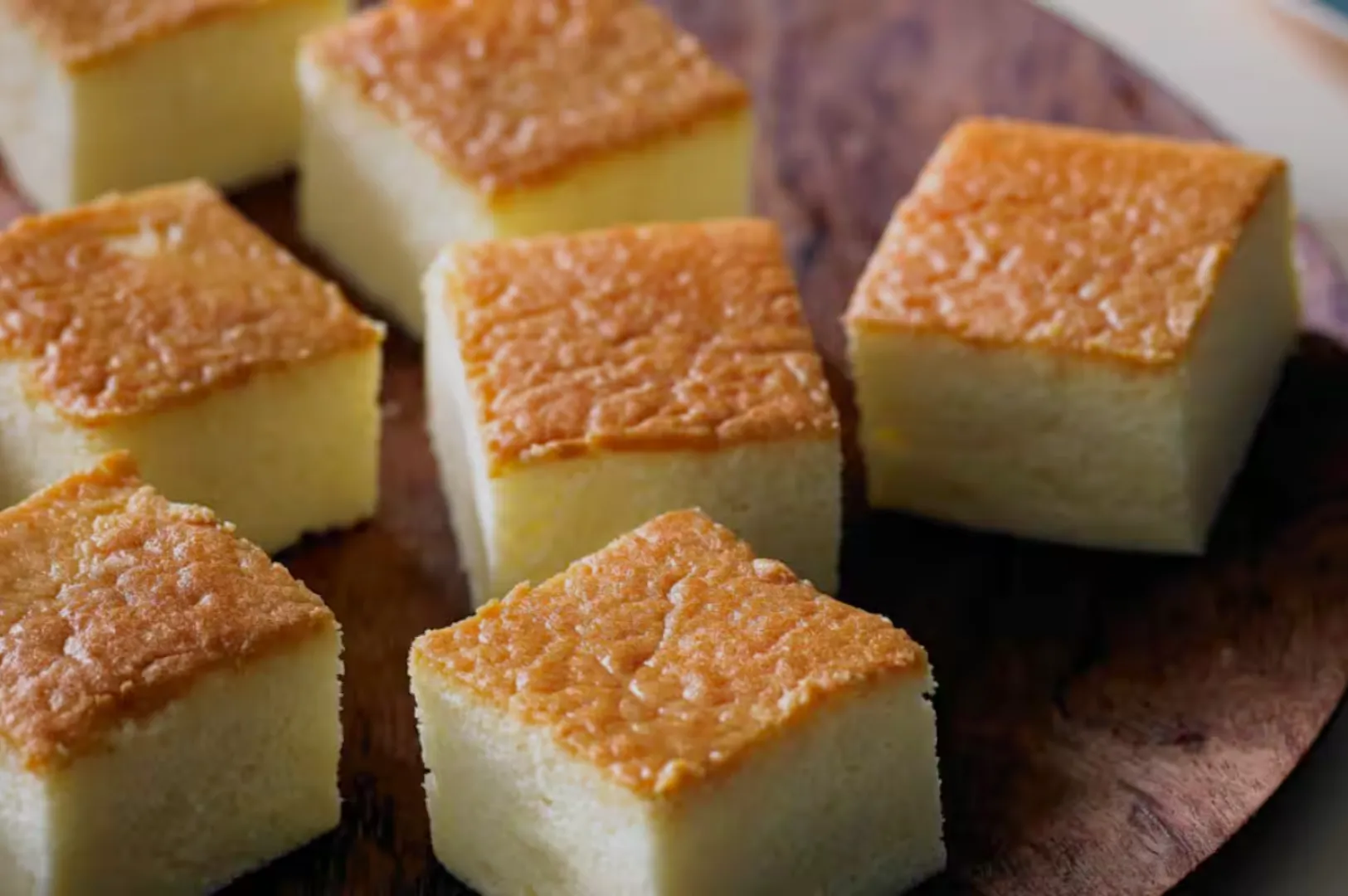 A close-up of several pieces of baked dessert squares with a golden brown top, placed on a wooden platter.