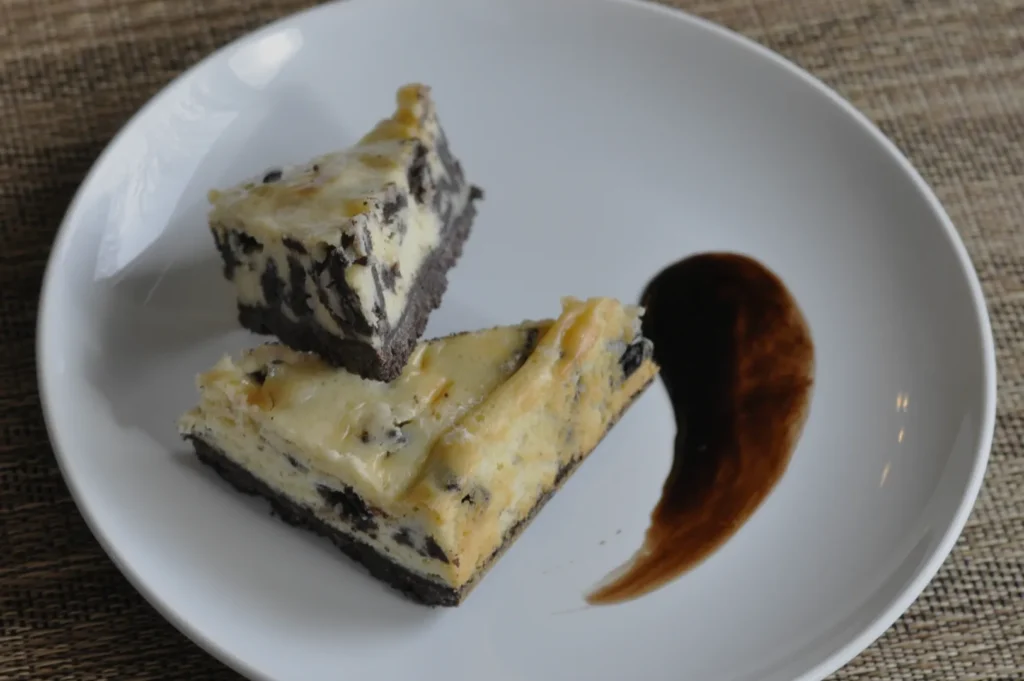 A plate with two slices of cheesecake, one partially eaten, with a dark sauce drizzled beside it.