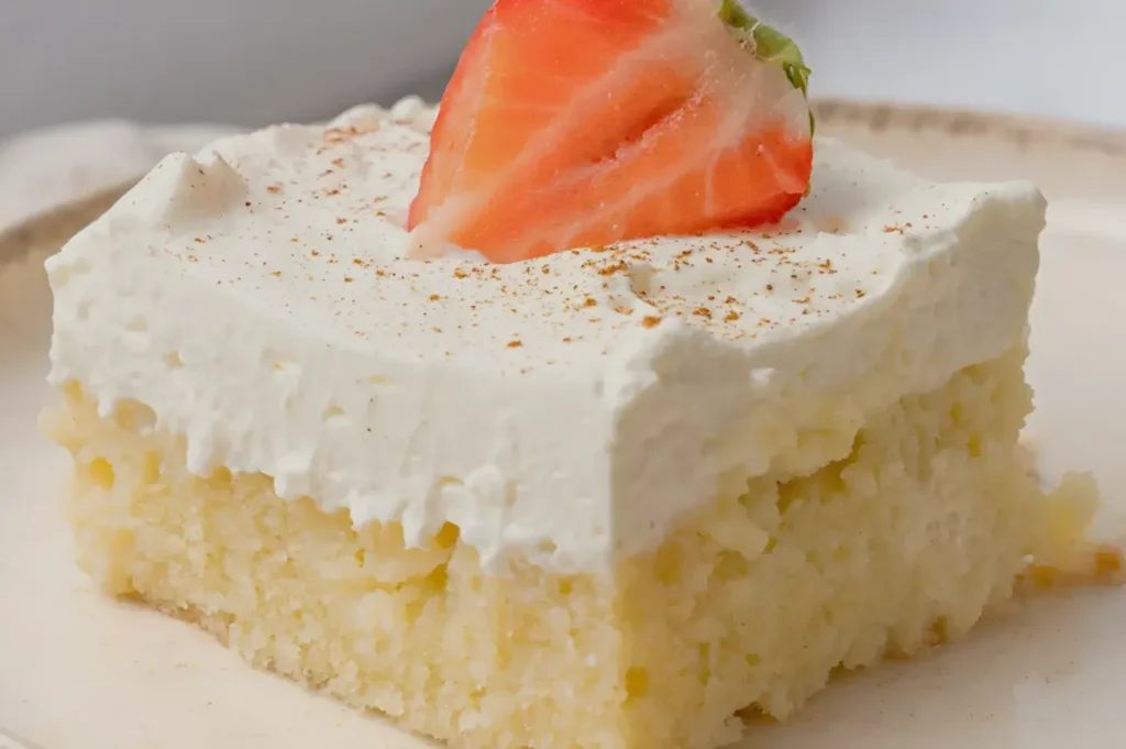A slice of coconut cream cake topped with a fresh strawberry and a sprinkle of cinnamon.