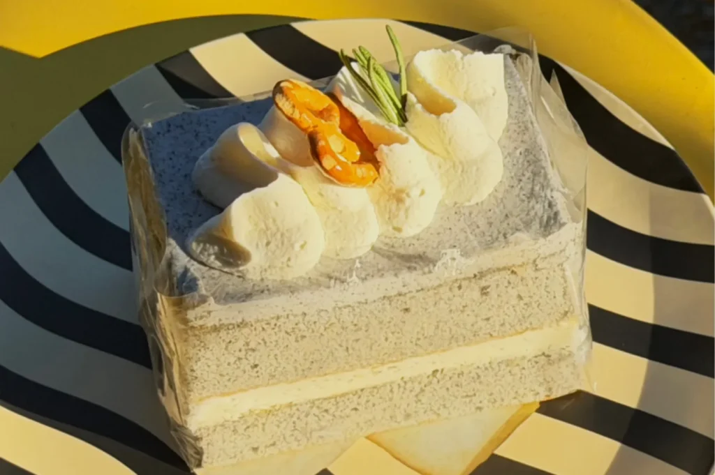 A slice of cake with a black and white design, topped with cream and a slice of fruit, sitting on a striped plate.