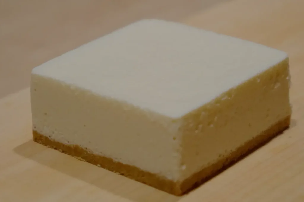 A rectangular piece of cheesecake with a graham cracker crust on the bottom.