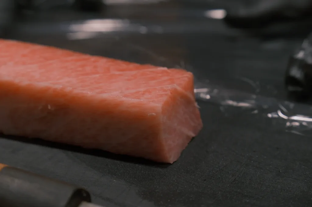 Close-up of a thick, glistening piece of marbled tuna on a dark surface, highlighting its fresh, rich texture and vibrant pink color.