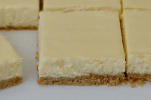 A close-up of sliced cheesecake on a white plate, showcasing a smooth creamy top and a crumbly crust.