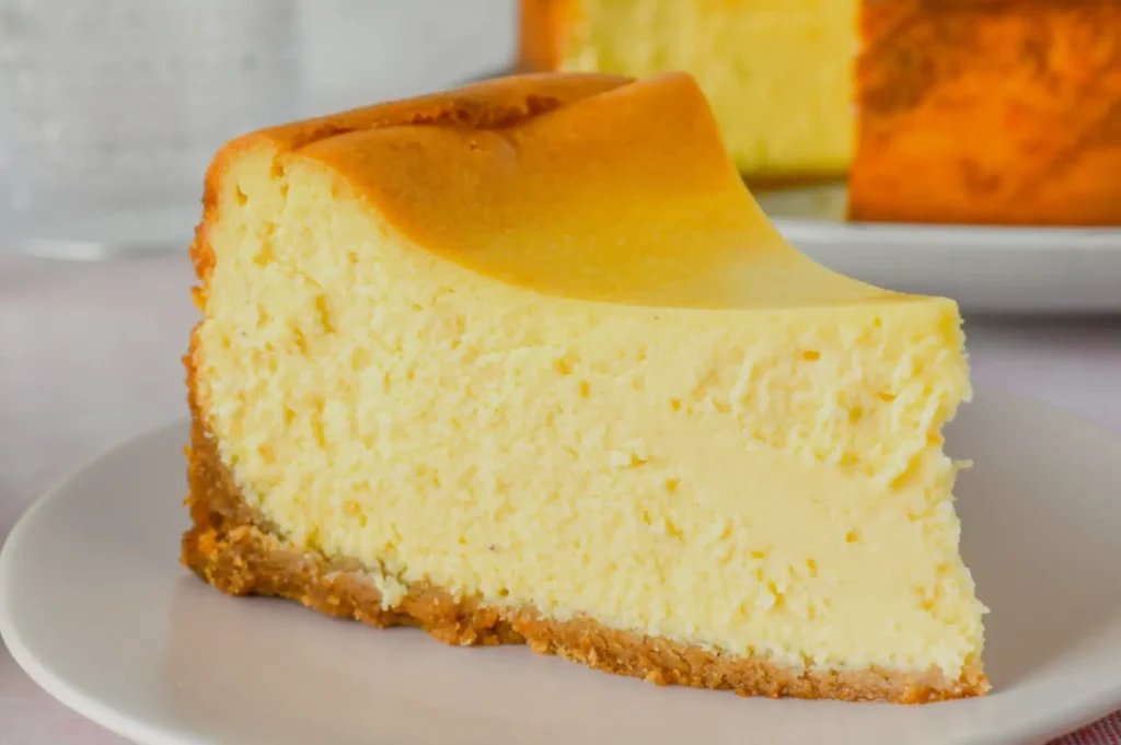 A slice of new york cheesecake on a plate, showing a creamy texture and a golden-brown crust.
