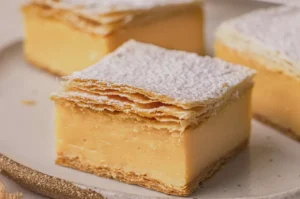 A close-up of a slice of mille-feuille, featuring layers of pastry and creamy filling, dusted with powdered sugar.