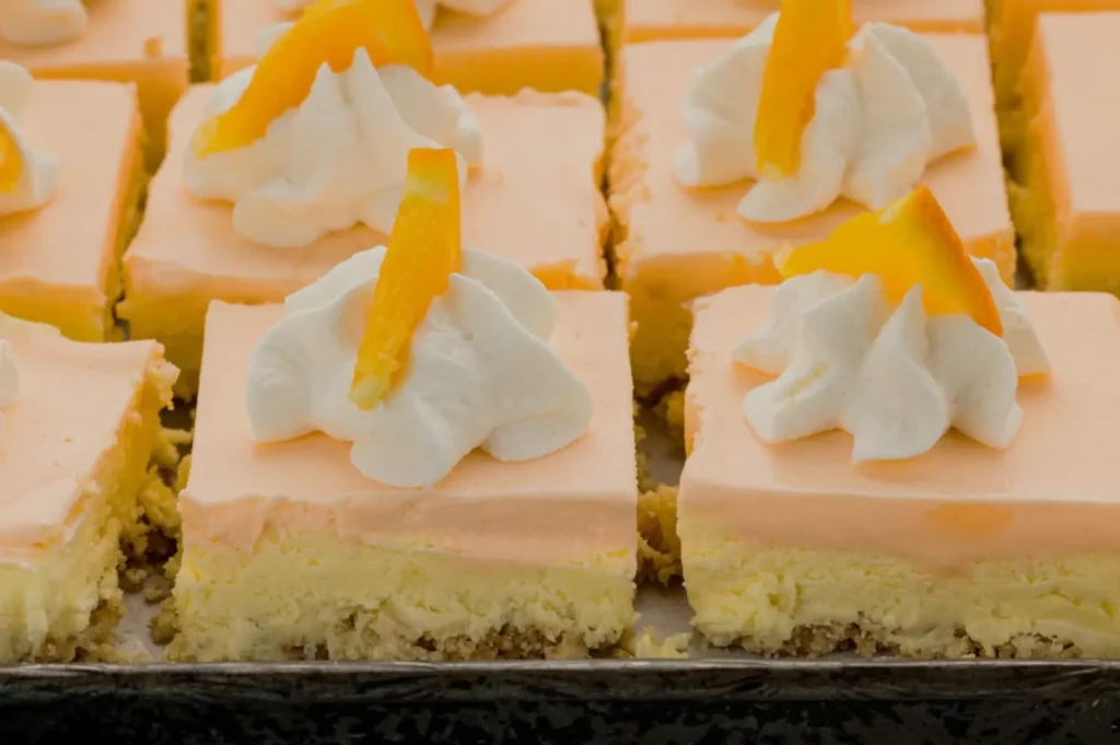 A tray of orange cheesecake squares topped with whipped cream and orange zest.