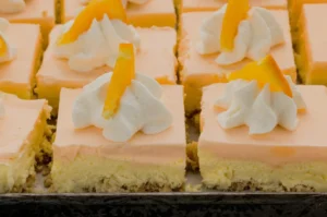 A tray of orange cheesecake squares topped with whipped cream and orange zest.