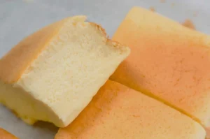 A close-up of fluffy, light yellow cake squares with a slightly browned top. One square has a bite taken out of it.