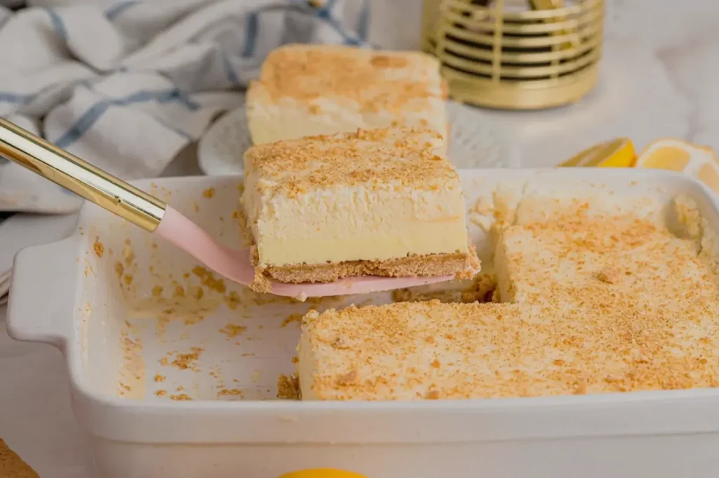 A dessert with a graham cracker crust and creamy topping, displayed in a dish with a spatula serving a piece.