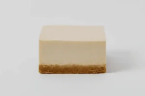 A rectangular piece of cheesecake with a smooth, creamy top layer and a crumbly base.