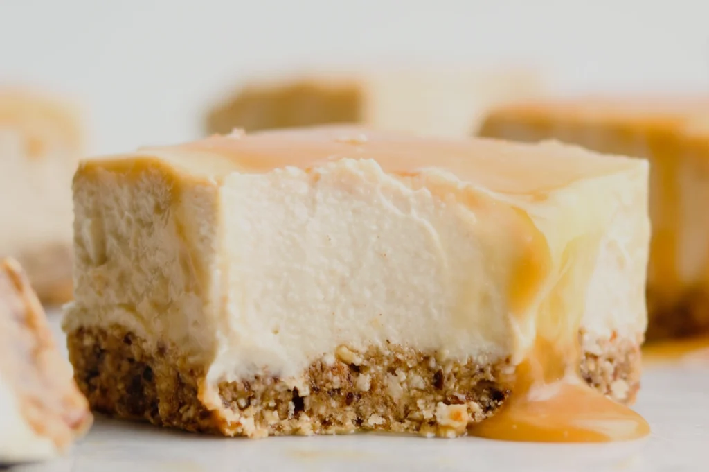 A close-up of a creamy dessert with a graham cracker crust, topped with a layer of caramel drizzle.