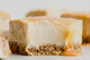 A close-up of a creamy dessert with a graham cracker crust, topped with a layer of caramel drizzle.